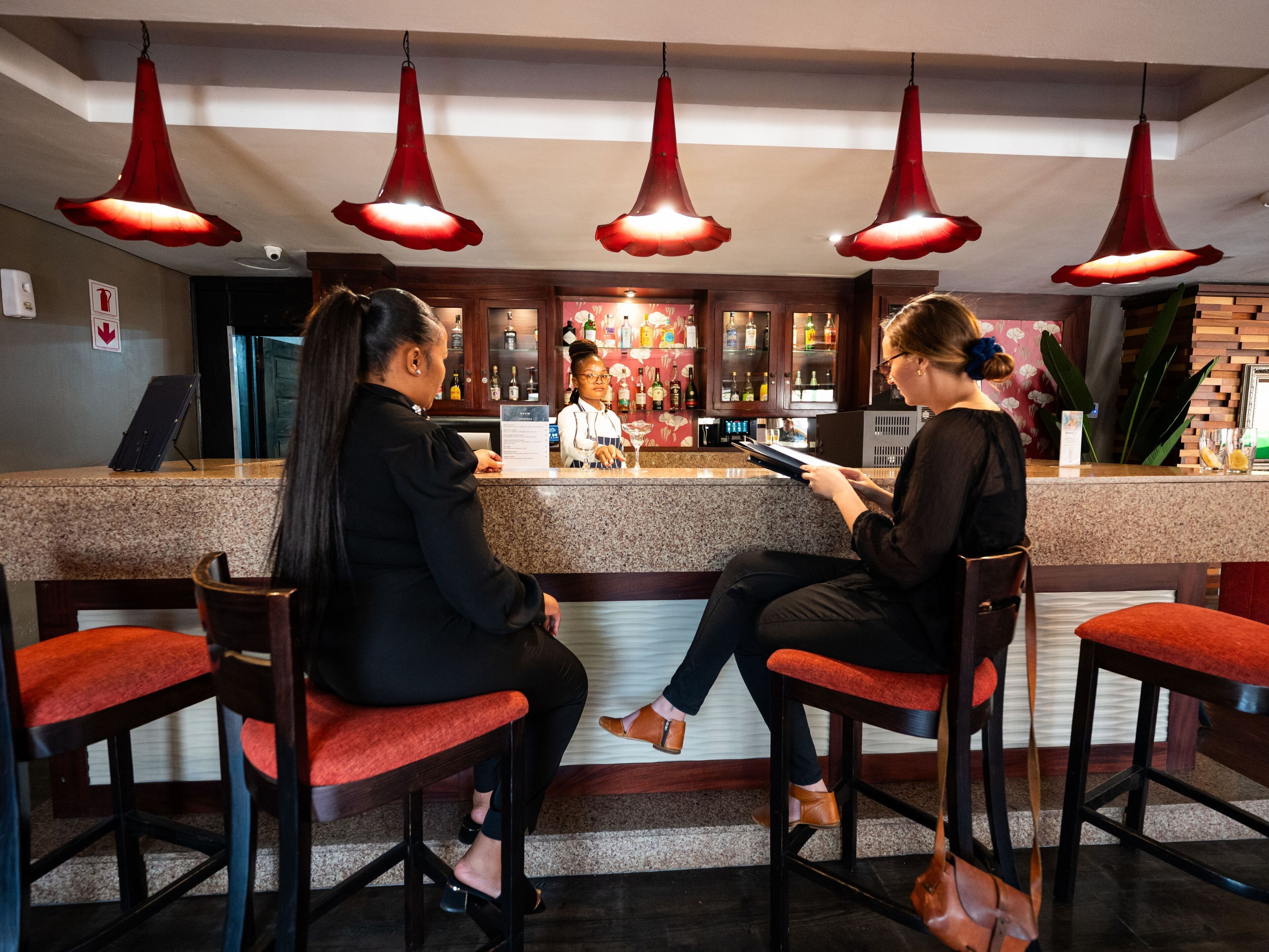 Un espace bar avec un comptoir, des suspensions rouges et des sièges.