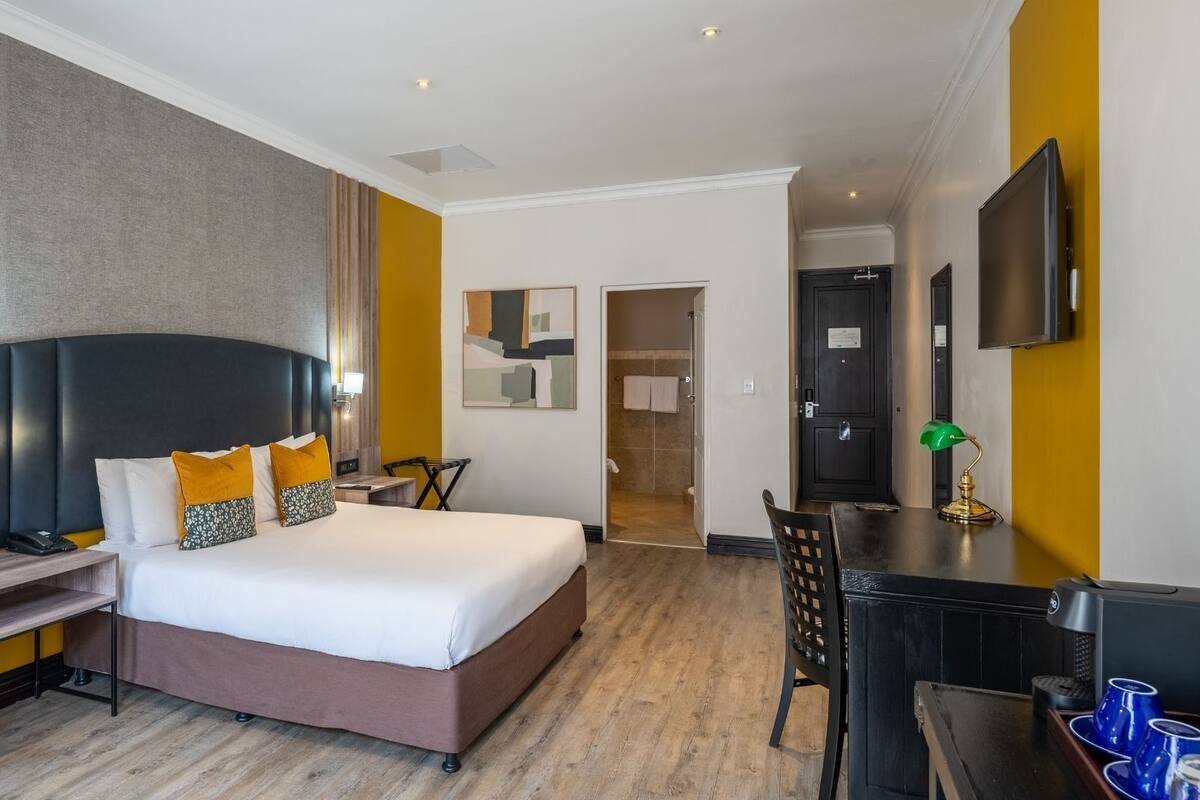 A hotel room with a bed, bedside table, desk, chair, and a television.