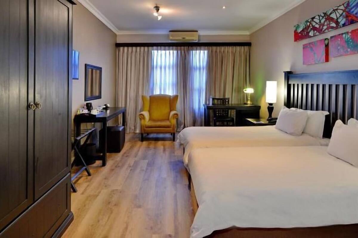 A hotel room with a large bed, a desk, a chair, and a wardrobe.