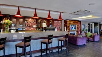 Een bar met een toonbank, krukken en een zithoek met een bank en stoelen.
