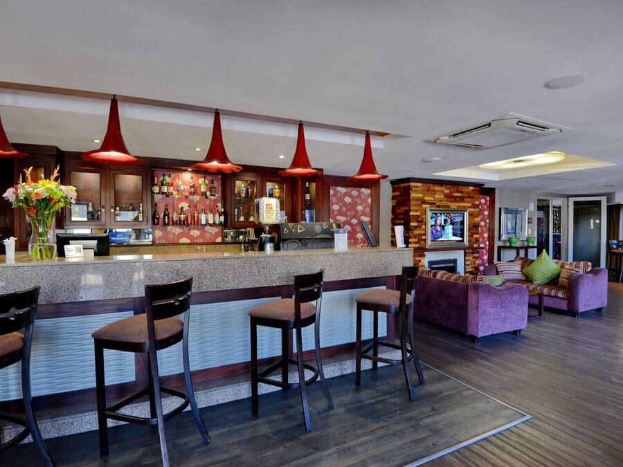 Een bar met een toonbank, krukken en een zithoek met een bank en stoelen.