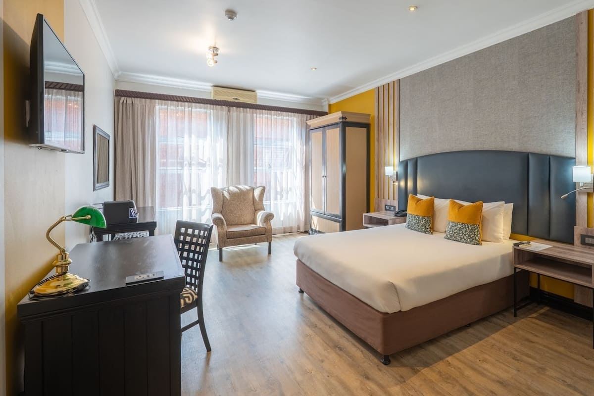 A hotel room with a bed, a desk, a chair, a TV, and a large window with curtains.
