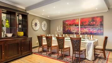 A dining area with a table set for six, surrounded by patterned chairs, a dark wooden cabinet with glass doors, and two decorative wall mirrors.
