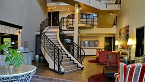Eine großzügige Lobby mit einer imposanten Treppe, einem Empfangsbereich und einer Sitzecke mit gemusterten Stühlen.