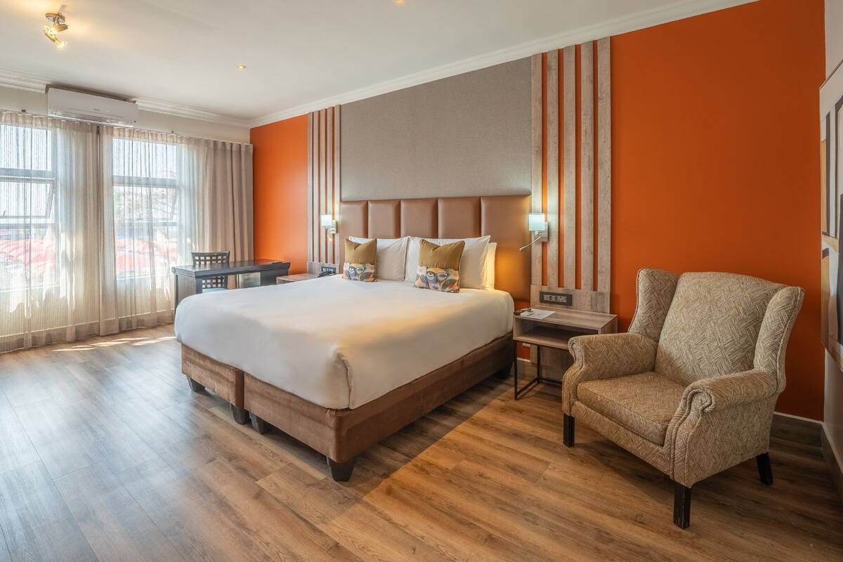A hotel room with a large bed, a desk, a chair, and a view of the outside through the window.