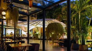 An outdoor dining area with tables and chairs, a large umbrella, and potted plants. - Tribe Hotel (Nairobi)