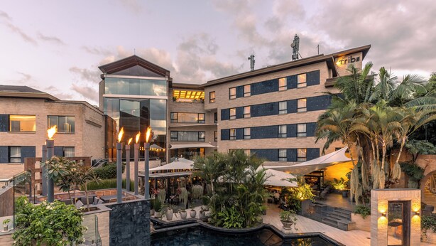 A hotel courtyard with a swimming pool, outdoor seating, and a modern building with a glass facade. - Tribe Hotel (Nairobi)
