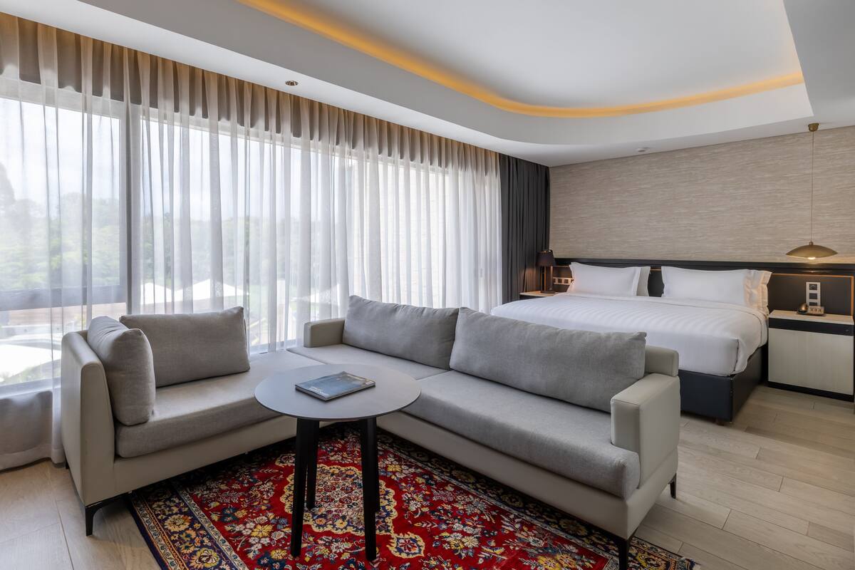 Moderni hotellihuone, jossa on suuri sänky, sohva, pieni pöytä ja yöpöytä.