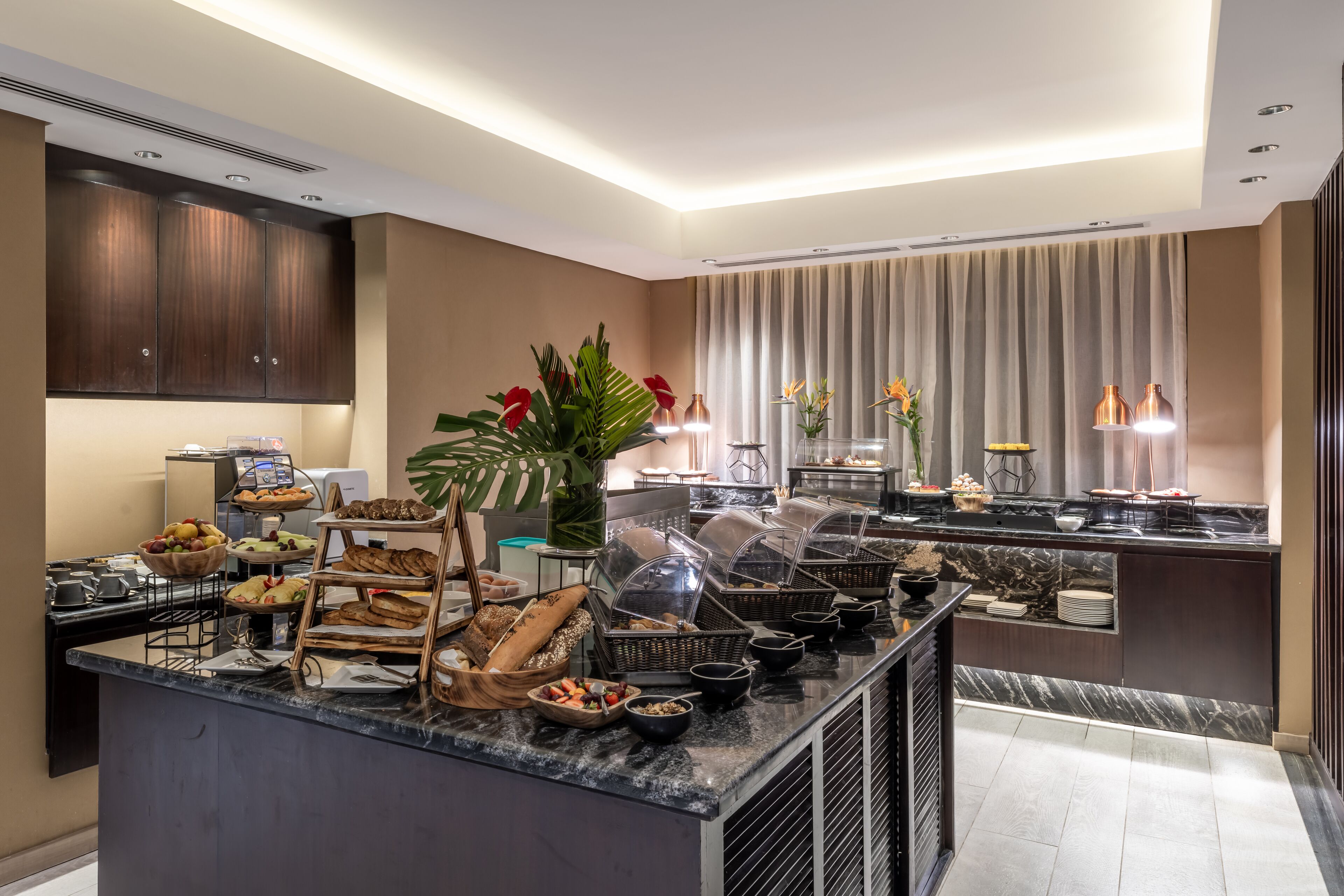 Cozinha moderna com bancada de mármore, mesa de buffet e uma grande janela com cortinas.