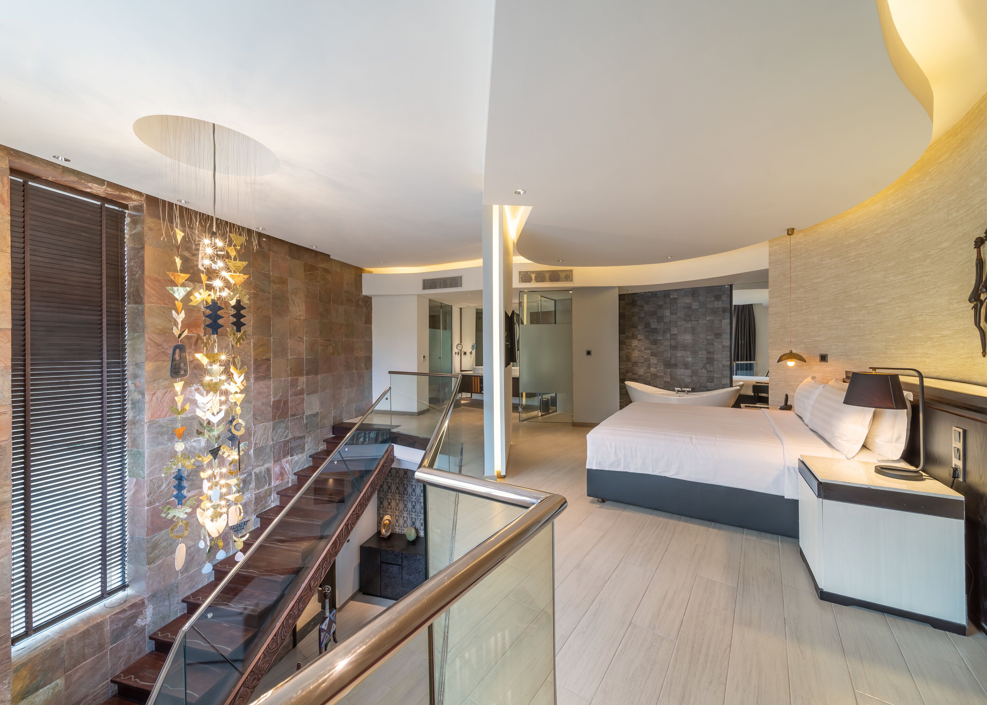 Ein modernes Hotelzimmer mit einem großen Bett, einer Sitzecke und einer Treppe mit dekorativer Beleuchtung.