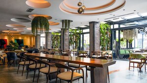A modern restaurant with wooden tables and chairs, hanging plants, and a unique ceiling design. - Tribe Hotel (Nairobi)