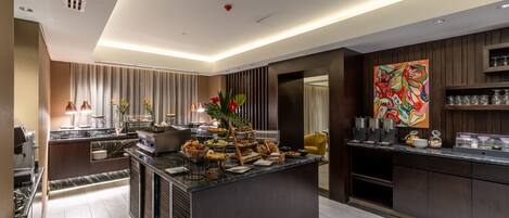 A modern kitchen with a marble countertop, a central island with food and drinks, and a large abstract painting on the wall.