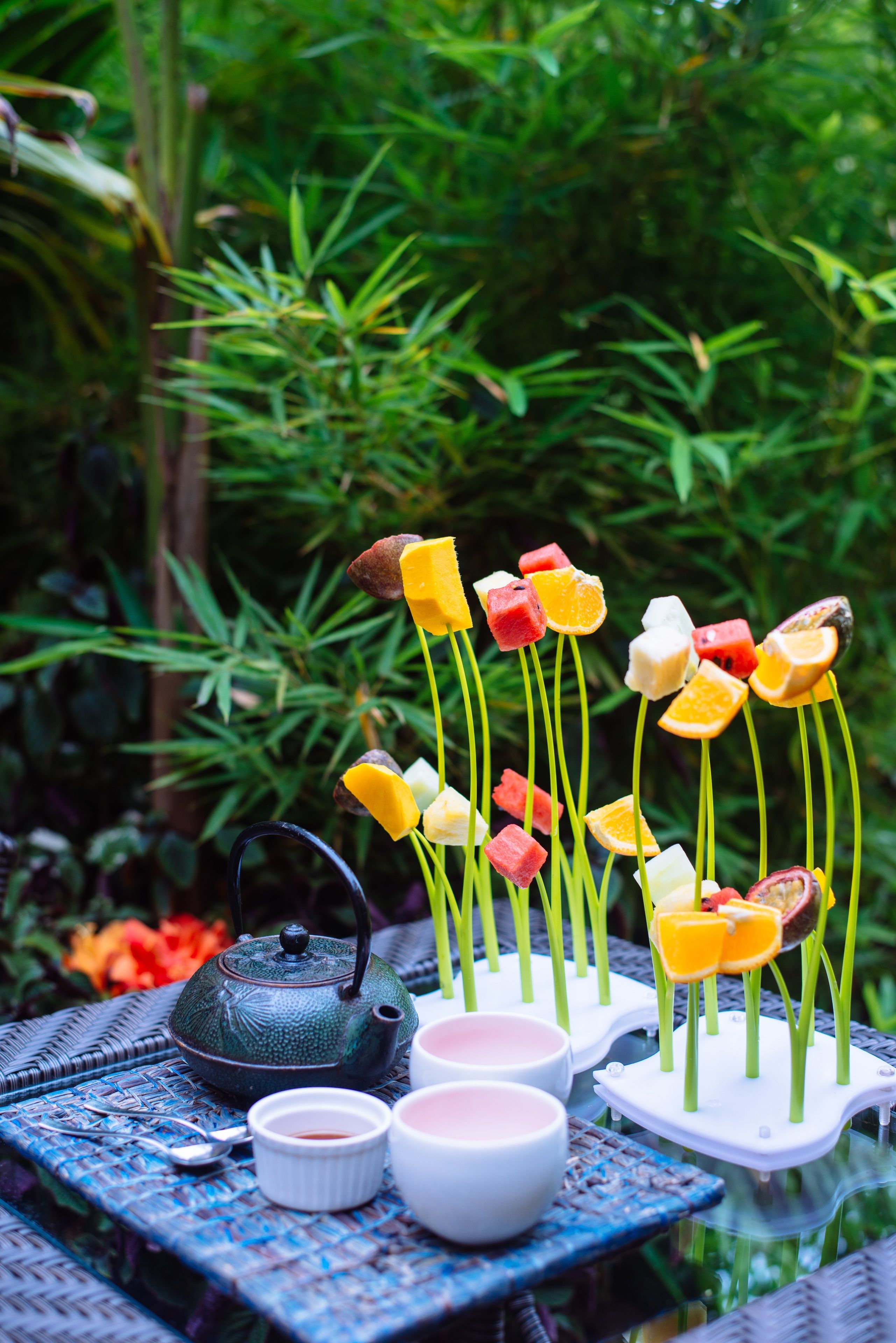 A table set with a teapot, cups, and fruit skewers.