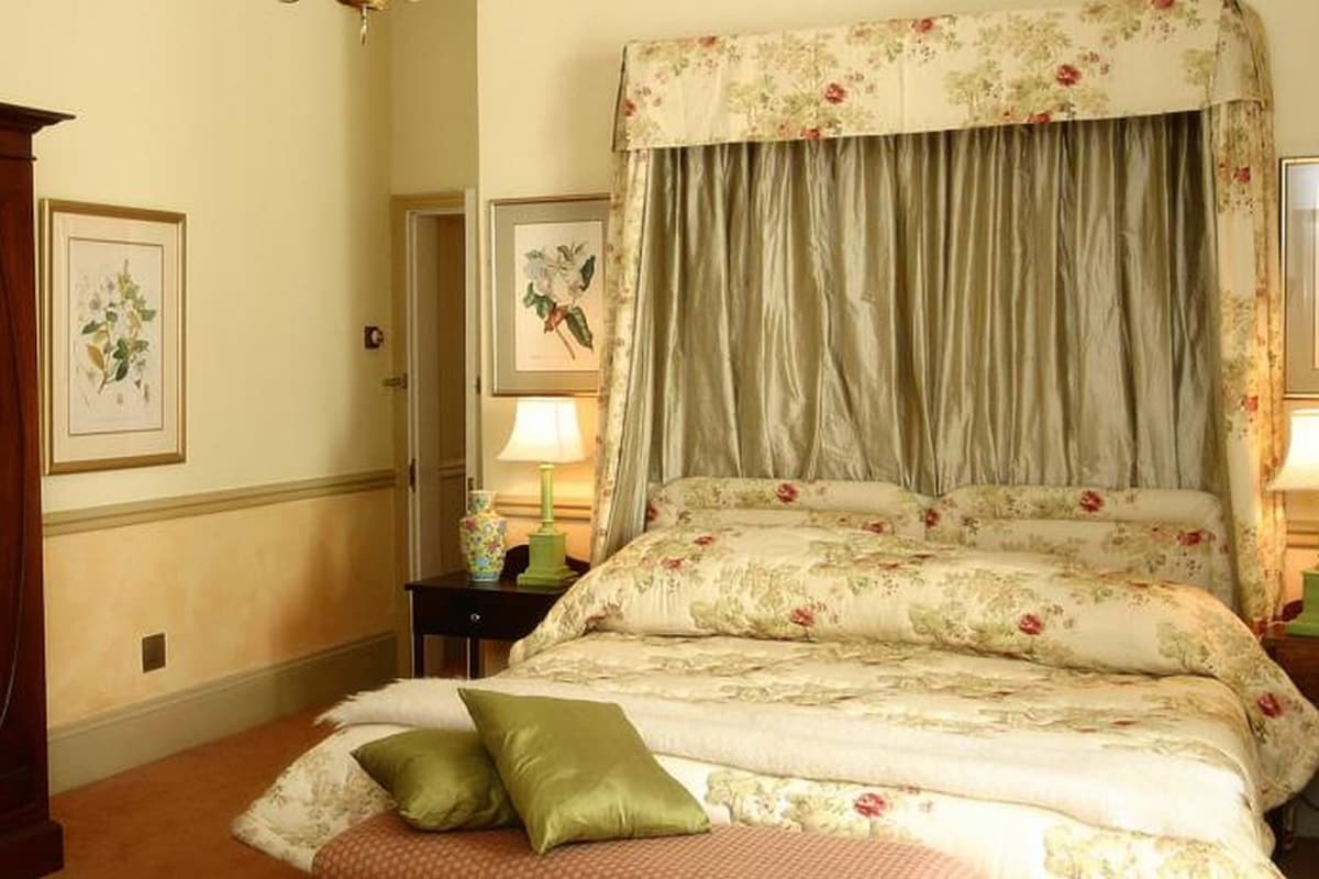 Ein Schlafzimmer mit einem Himmelbett, floralem Bettbezug, einem Holzschrank und zwei Nachttischlampen.