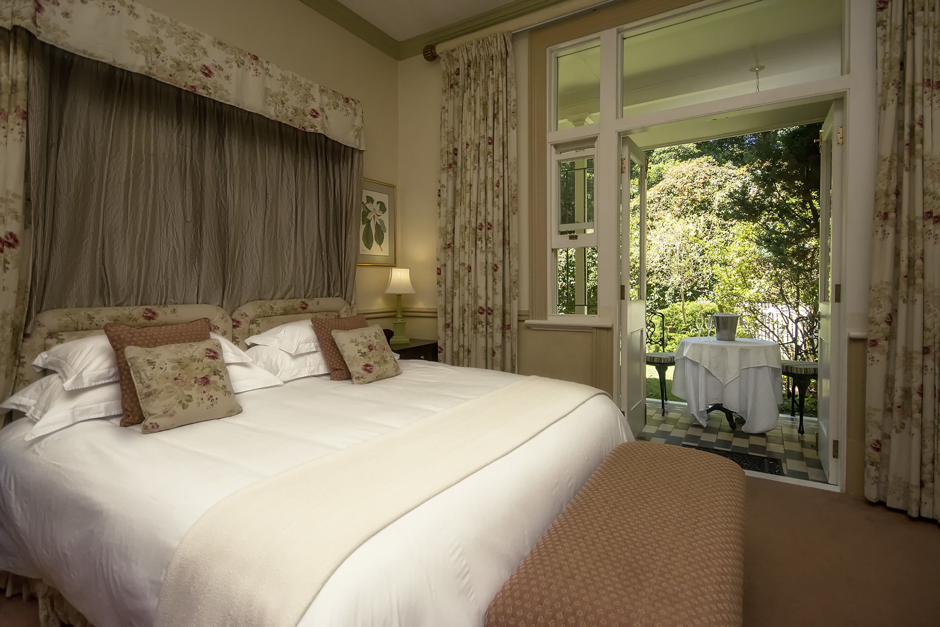 A large bed with floral curtains and a view of a garden through an open door.
