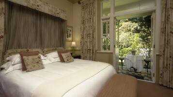 Una cama grande con cortinas florales y vistas a un jardín desde una puerta abierta.