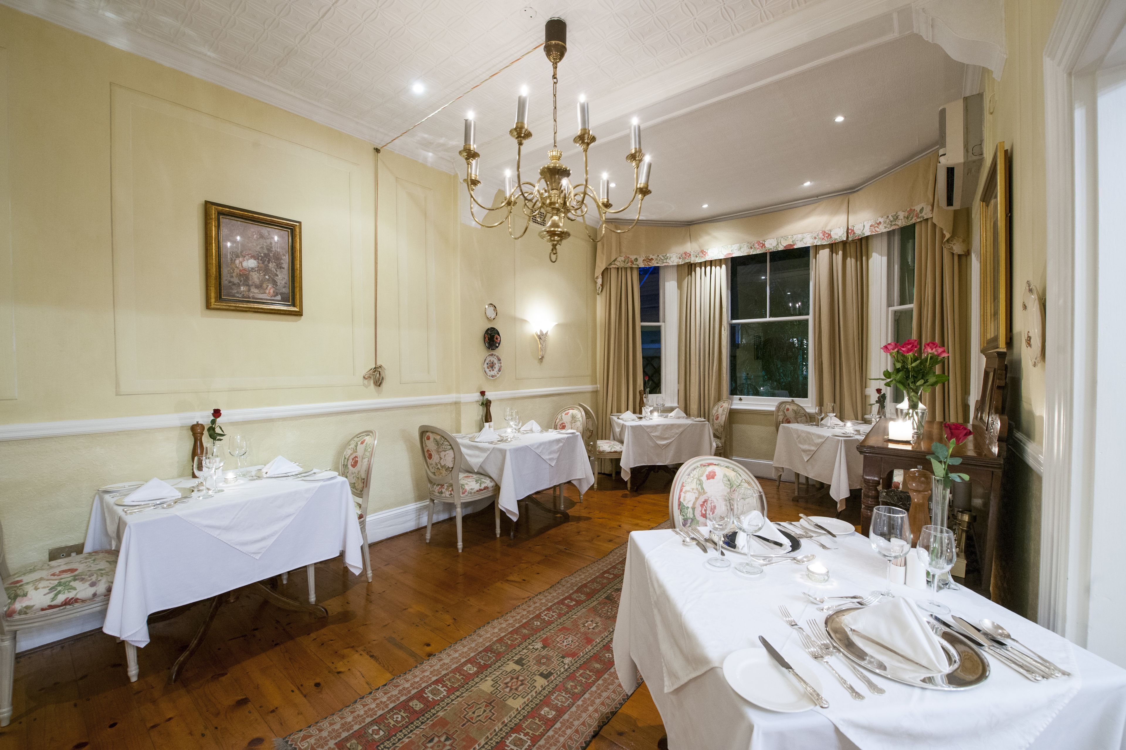 Un comedor con varias mesas dispuestas para una comida, con manteles blancos, sillas elegantes y un candelabro.