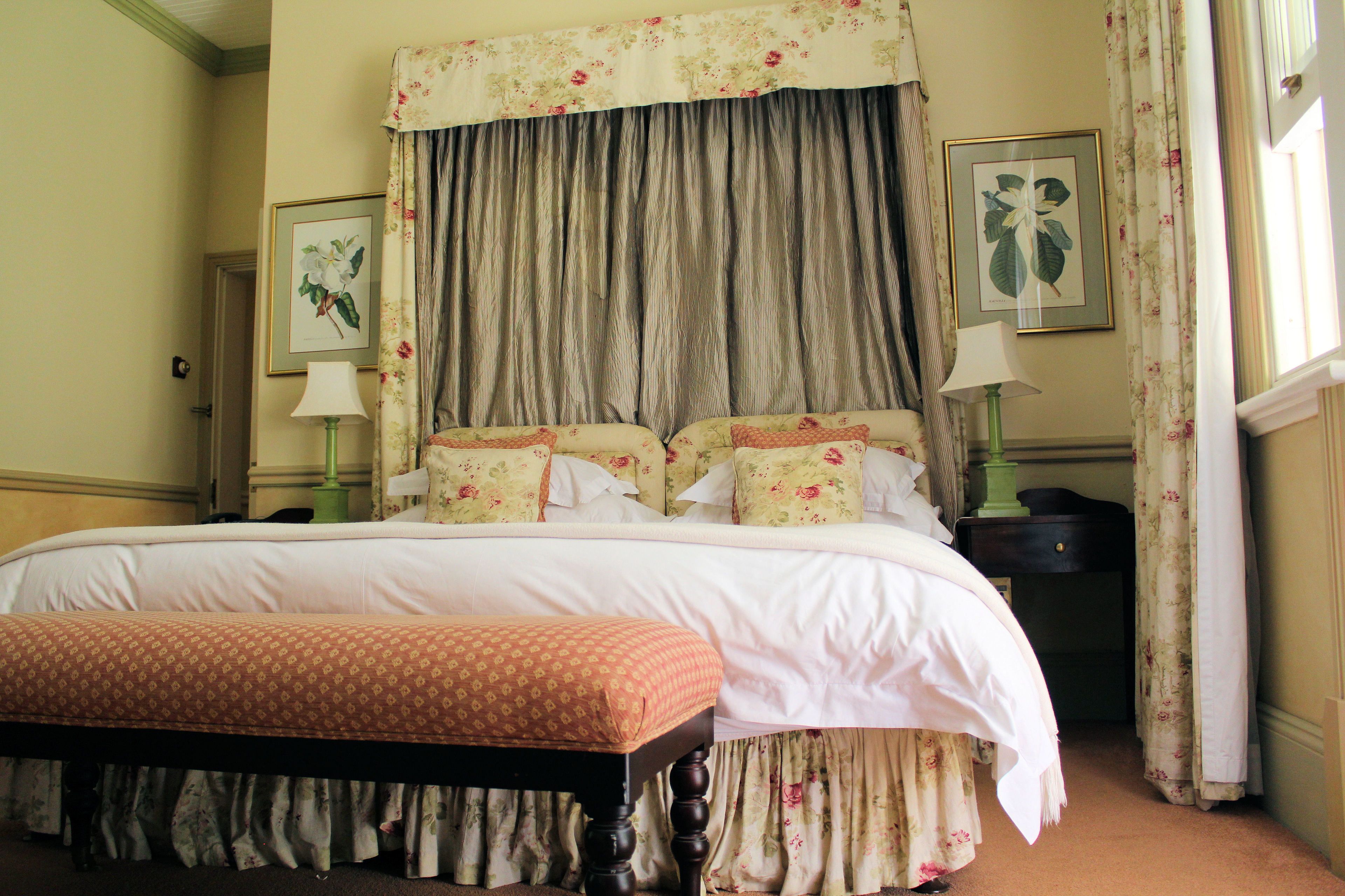 A neatly made bed with a floral bedspread, a matching bench, and a large window with curtains.
