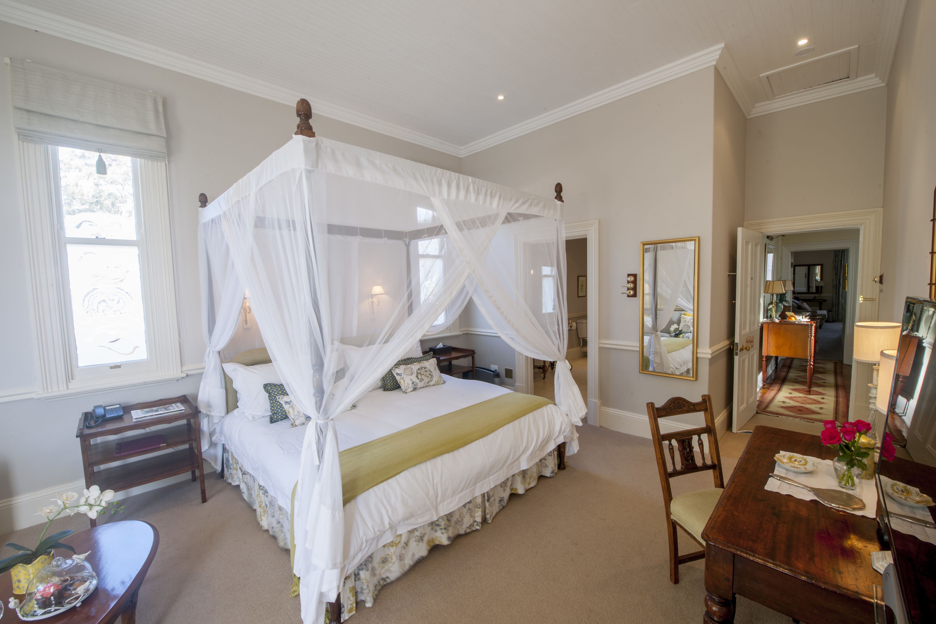 A bedroom with a four-poster bed, a wooden nightstand, a dining table with chairs, and a mirror on the wall.