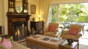 Uma sala de estar acolhedora com lareira, poltronas florais e vista para o exterior.