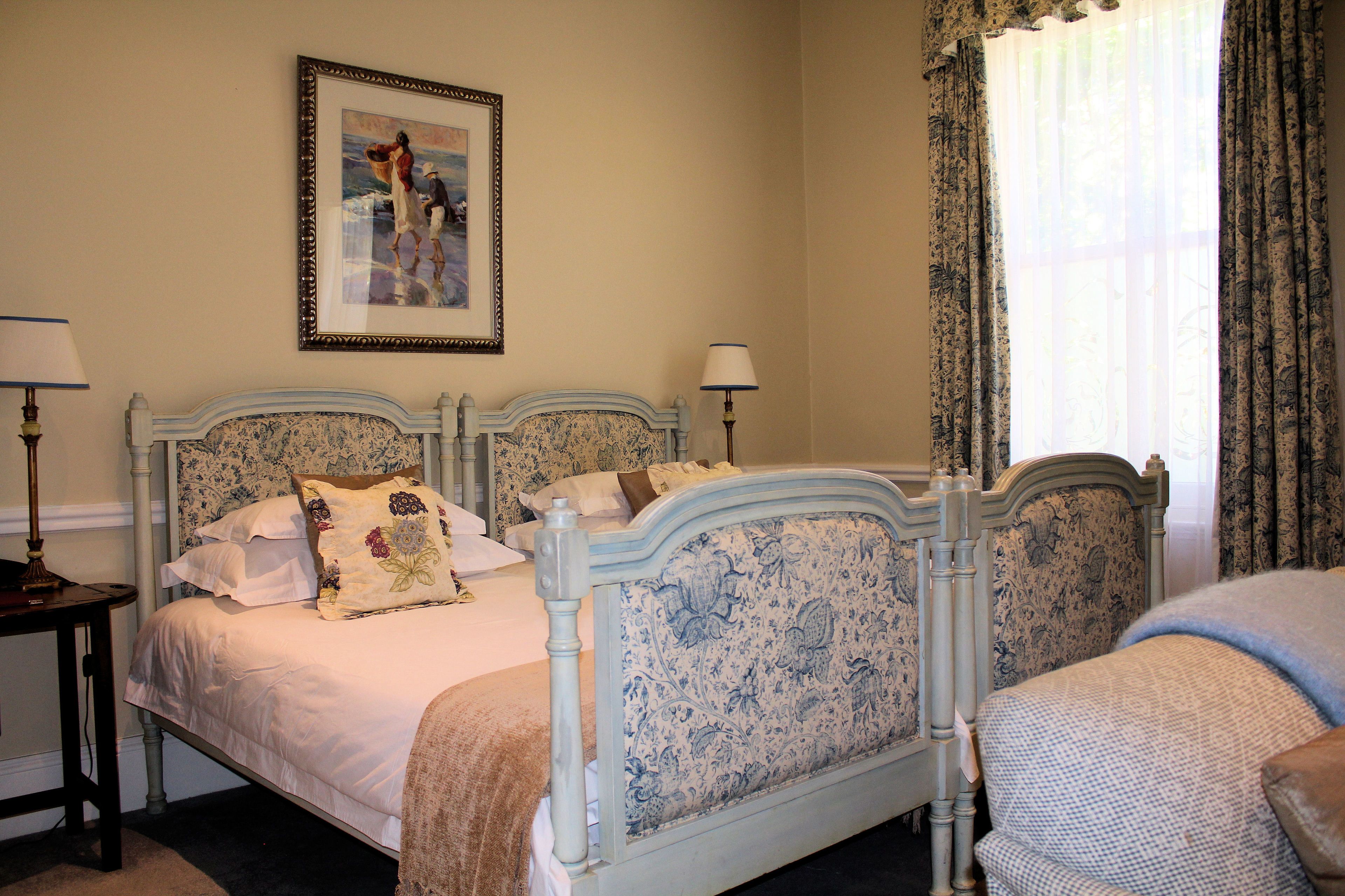 A bedroom with two beds, each with a headboard and a nightstand. There is a framed picture on the wall above the beds.