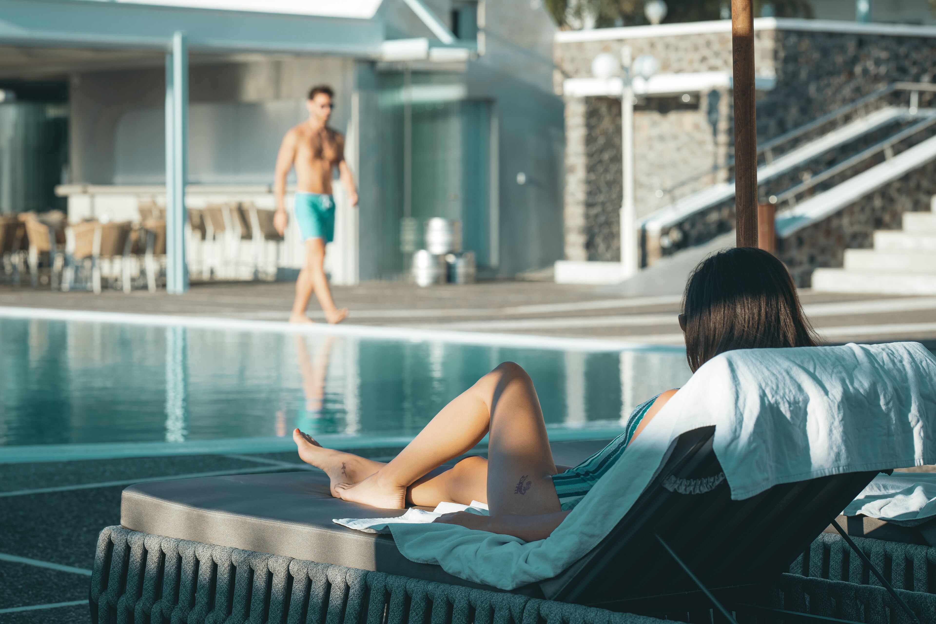 A poolside area with lounge chairs and a person relaxing by the pool.