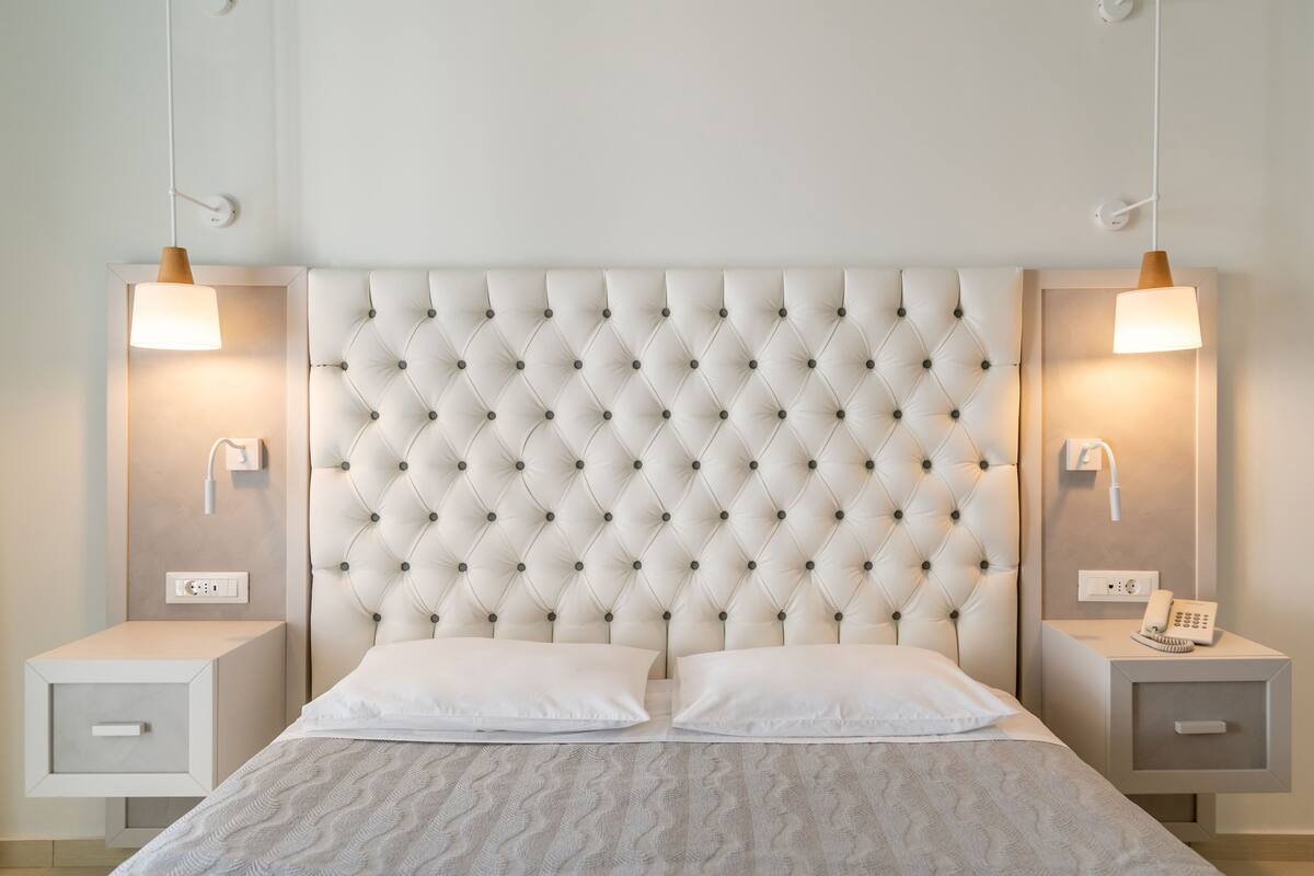 A bedroom with a tufted headboard, two bedside tables with lamps, and a bed with white bedding.