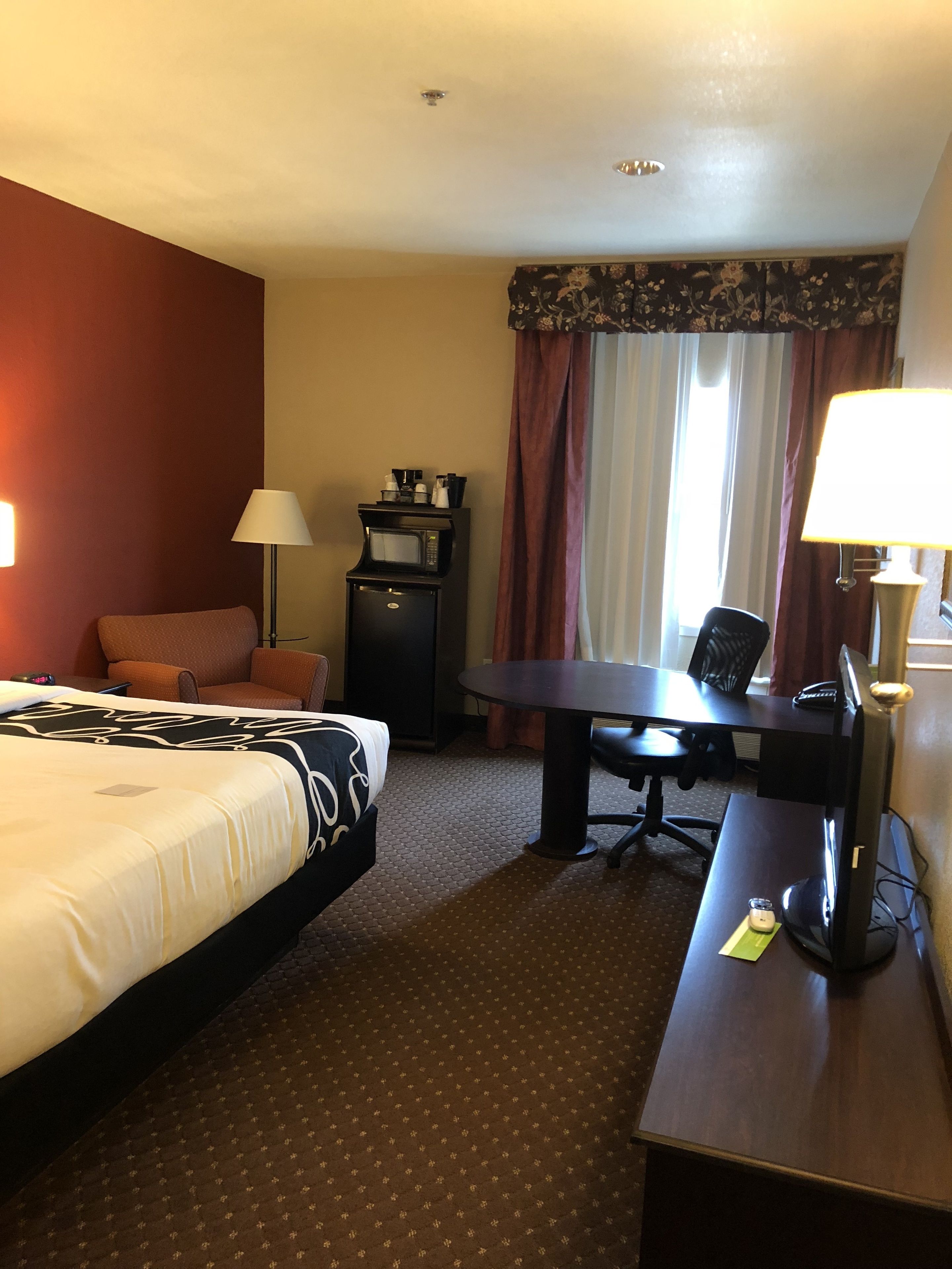 Habitación de hotel con cama, escritorio, silla, lámpara, cafetera y microondas.