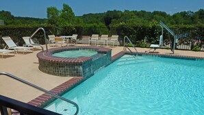 Una piscina con una vasca idromassaggio, circondata da sedie a sdraio e una recinzione.