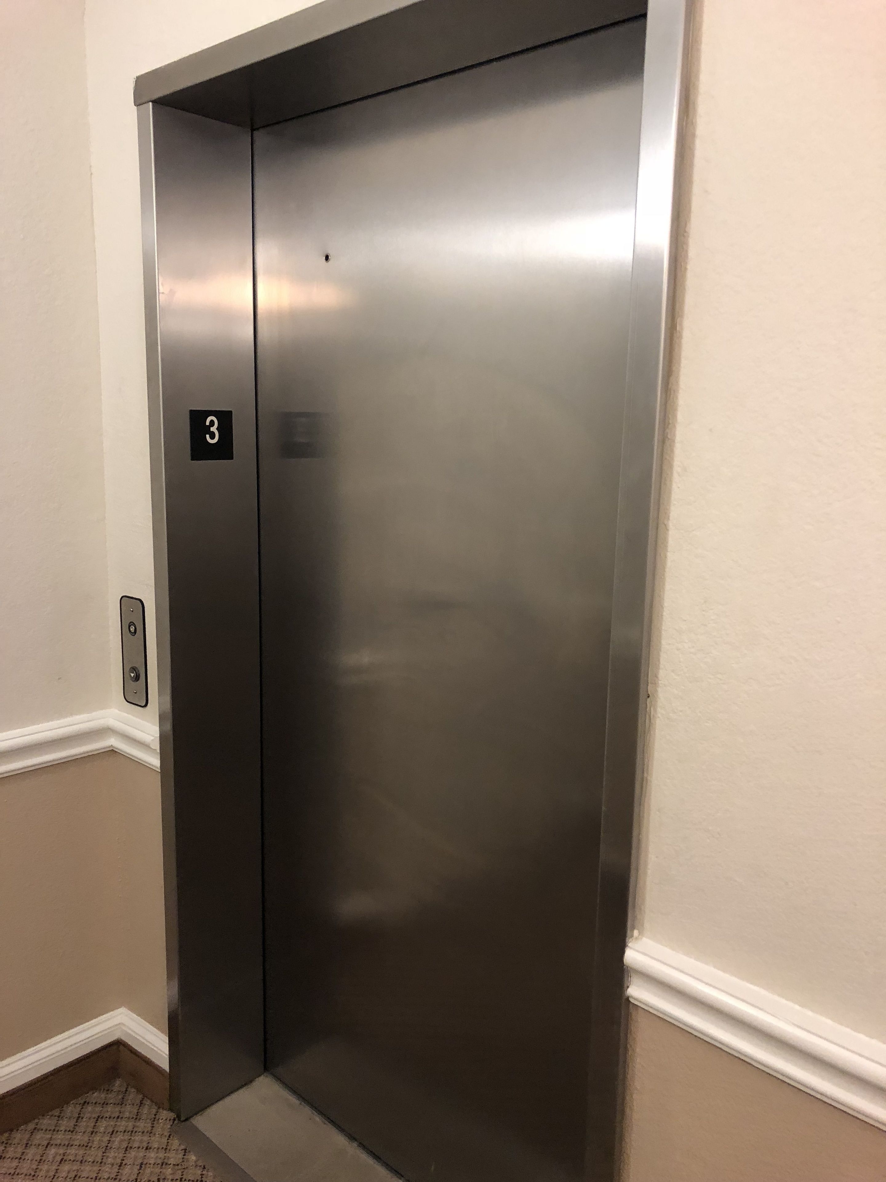 Une porte d’ascenseur en métal, avec une plaque indiquant qu’il s’agit du troisième étage.