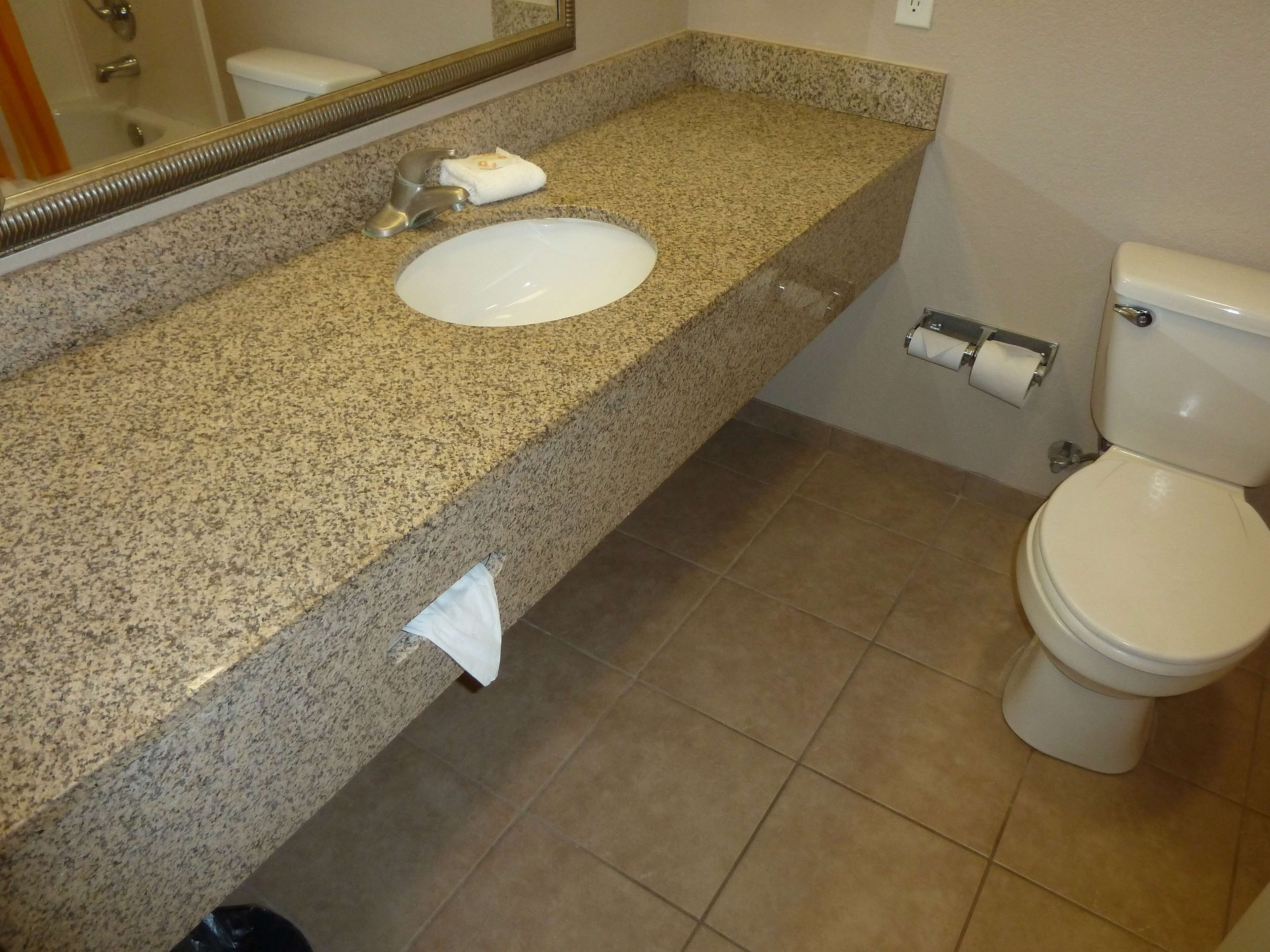 Un baño con encimera de granito, lavamanos blanco, inodoro y espejo.