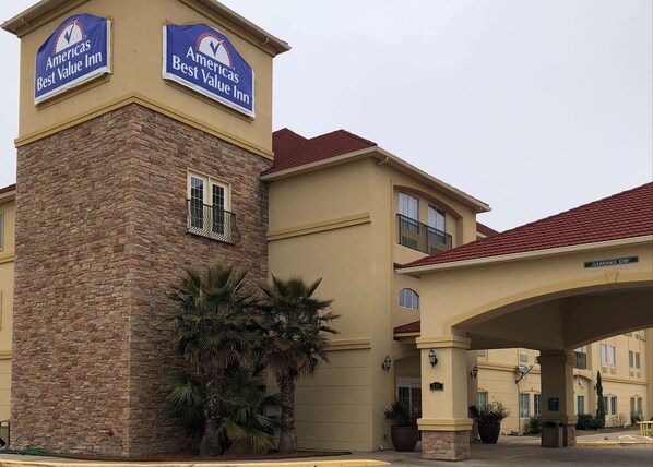 A Best Value Inn with a stone facade, a red-tiled roof, and a clear sign indicating a 1200' clearance. - Americas Best Value Inn & Suites Gun Barrel City (Mabank)