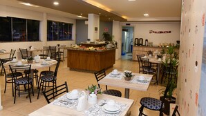 Un comedor de hotel con varias mesas y sillas, una estación de buffet central y un mostrador de recepción.