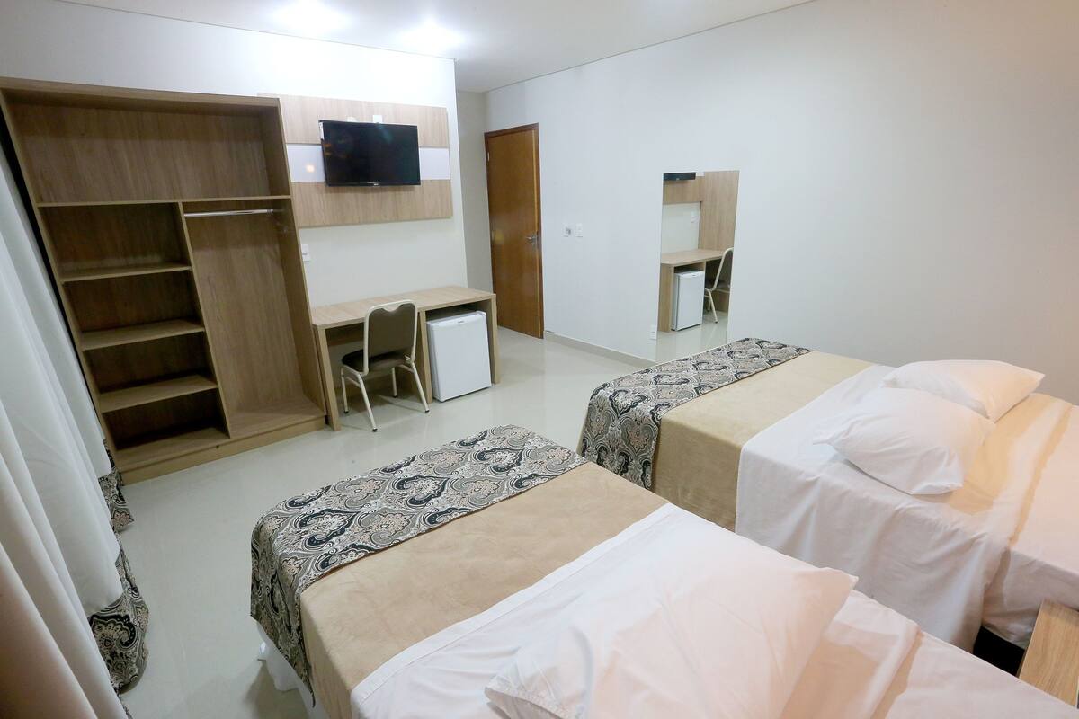 Quarto de hotel com duas camas, uma escrivaninha, um guarda-roupa e uma televisão.