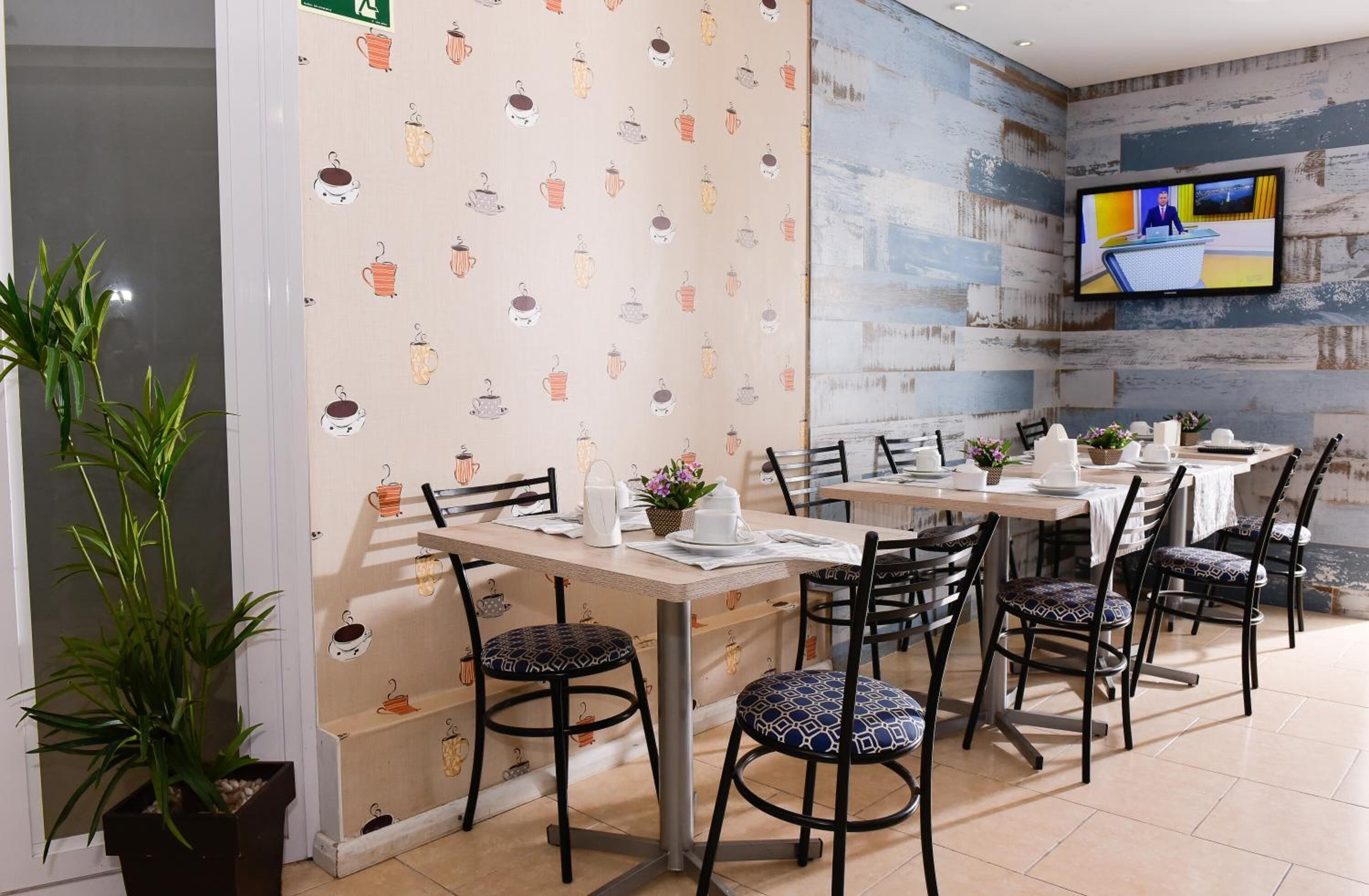 Un espace repas avec des tables et des chaises, un téléviseur fixé au mur et un papier peint à motifs.