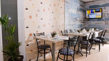 A dining area with tables and chairs, a television mounted on the wall, and a patterned wallpaper.