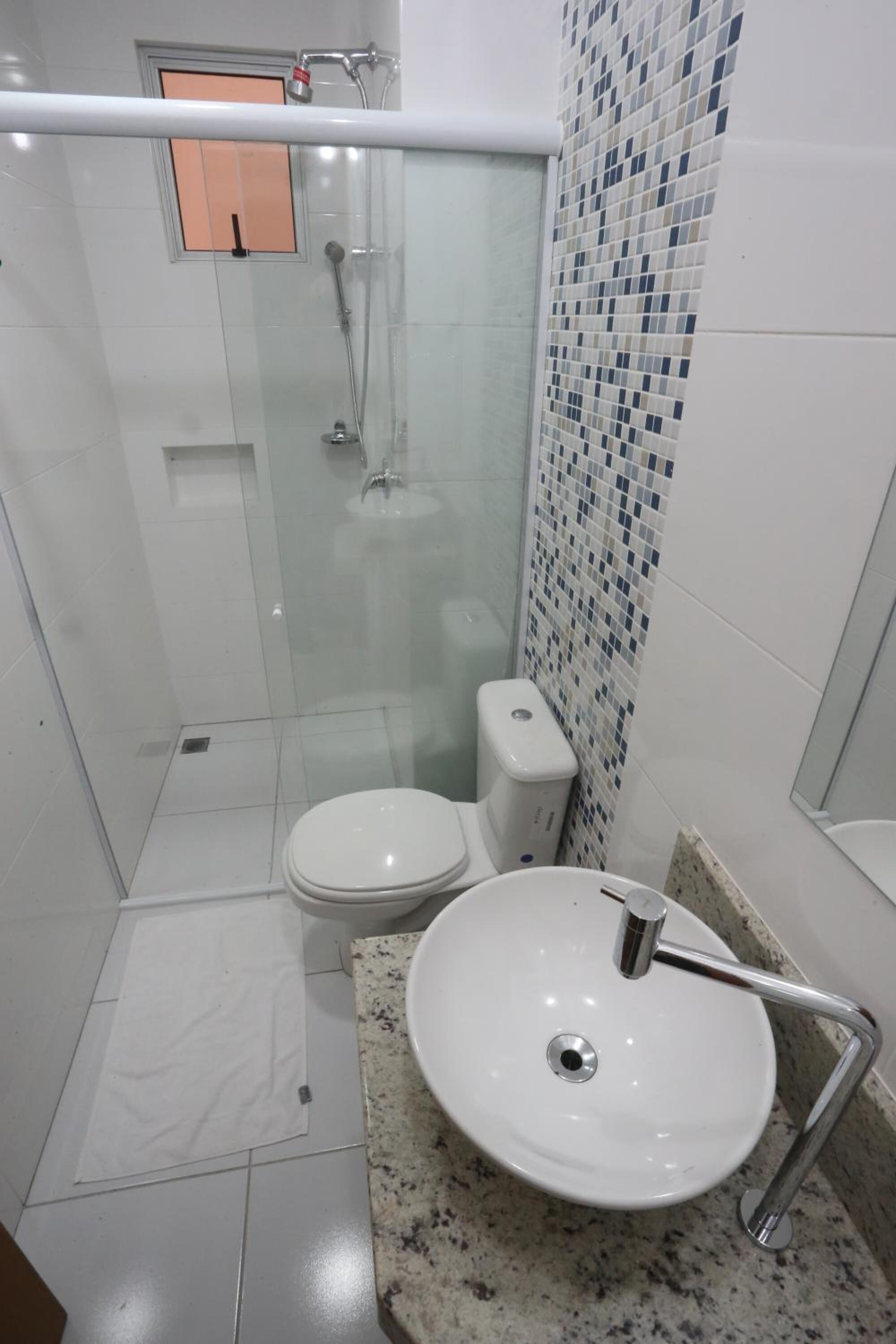 Een moderne badkamer met een douchecabine van glas, een wit toilet en een granieten aanrechtblad met een witte wastafel.