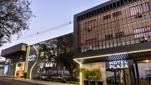Un hotel moderno con un llamativo letrero 'HOTEL PLAZA', una entrada visible y un área de estacionamiento.
