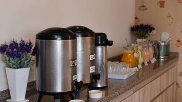 Stainless steel coffee urns labeled 'LEFT' and 'RIGHT' on a kitchen counter with a potted plant and a tray of condiments.