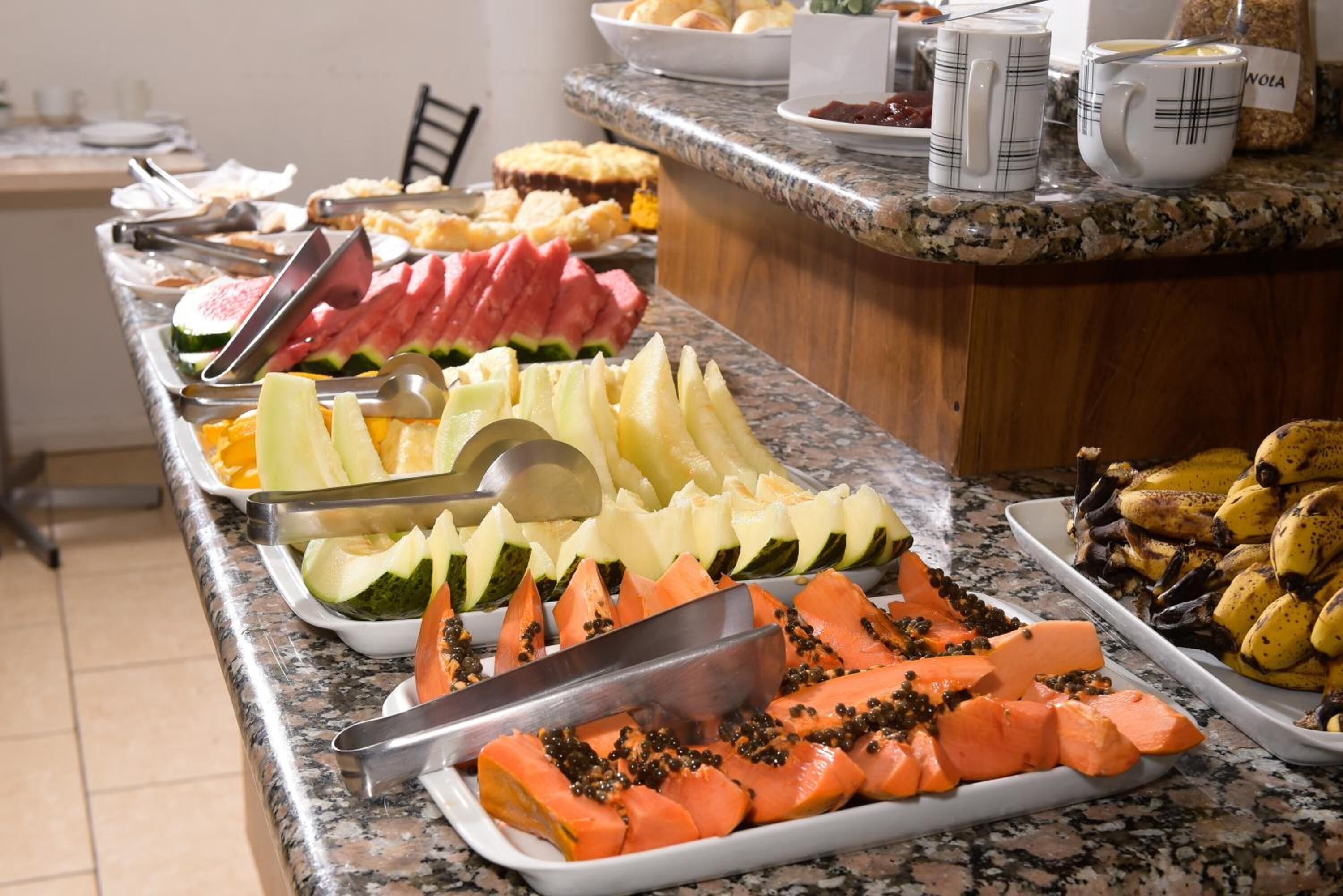 En buffet med et udvalg af frugter og grøntsager, herunder vandmelon, cantaloupe og gulerødder.
