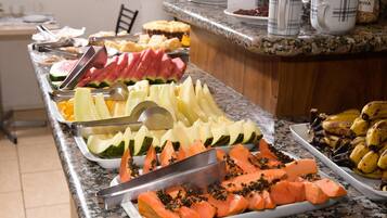En buffet med et udvalg af frugter og grøntsager, herunder vandmelon, cantaloupe og gulerødder.
