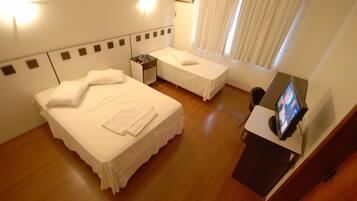 Una habitación de hotel con dos camas, un escritorio con televisor y una ventana con cortinas.