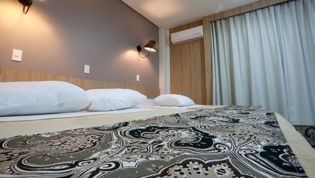 Una habitación de hotel con una cama, dos lámparas de pared y un ventanal con cortinas.