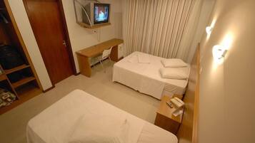 Quarto de hotel com uma cama, uma escrivaninha, televisão e um guarda-roupa.