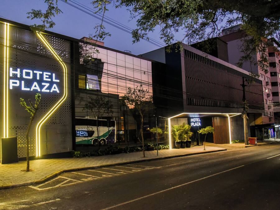 Een modern hotel met een opvallend neonreclamebord, een bushalte en een goed verlichte ingang.
