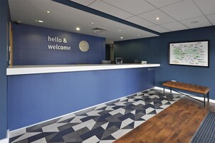 Un área de recepción con pared azul, un reloj, un mapa y un banco.