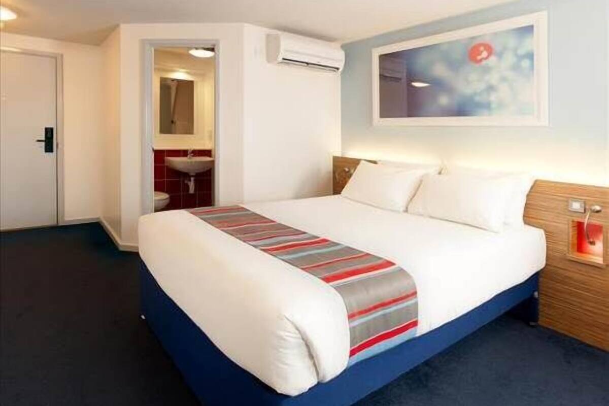 A hotel room with a bed, a bathroom, and a painting on the wall.