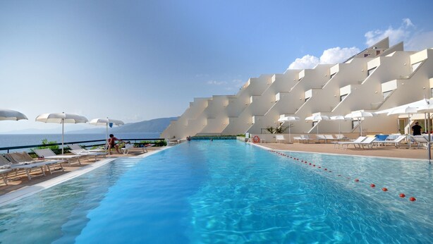 A swimming pool with sun loungers and umbrellas, a clear sky, and a mountainous backdrop. - Grand Hotel San Pietro (Centola)