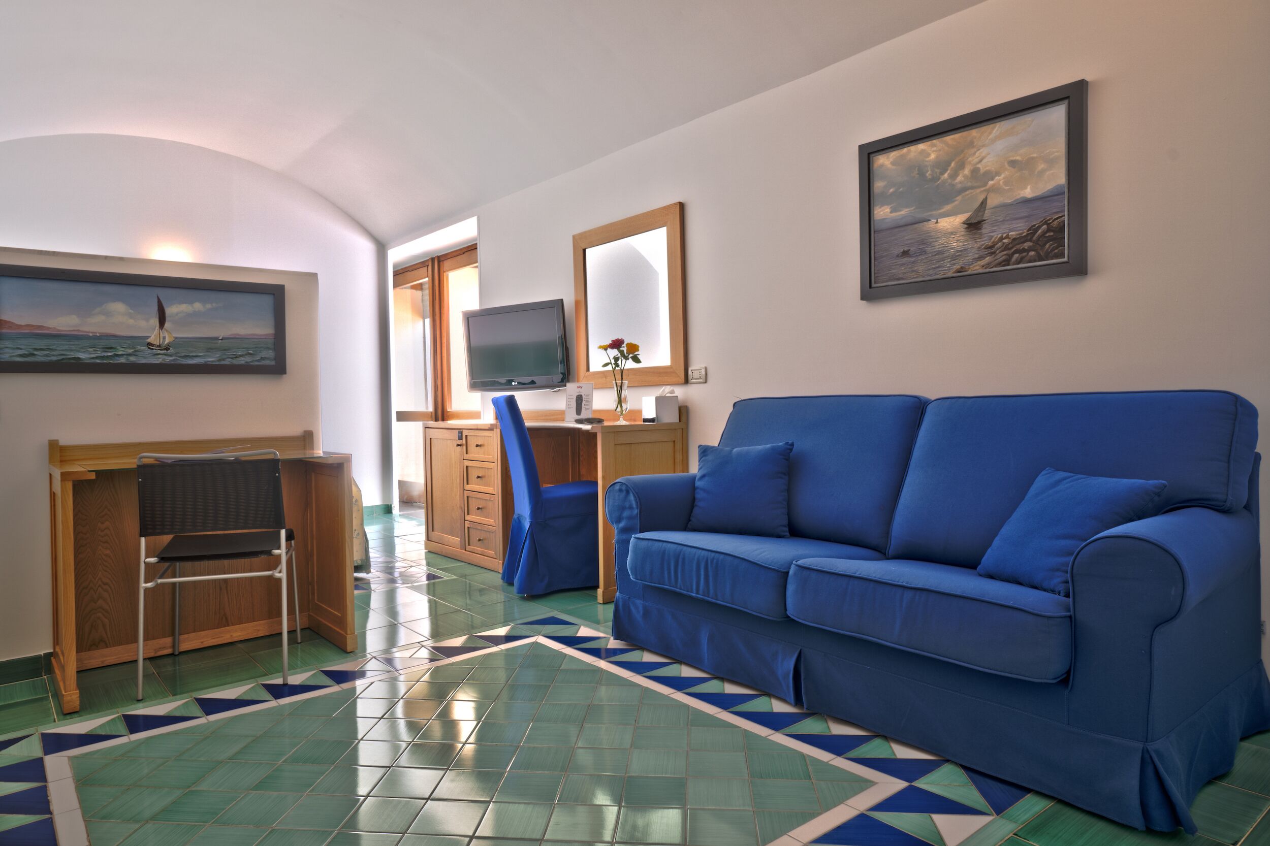 Un soggiorno con un divano blu, una scrivania in legno, un televisore e un quadro raffigurante una barca a vela.