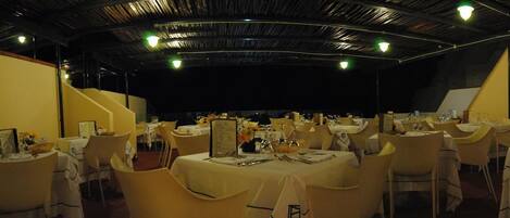 A banquet hall with round tables covered with white tablecloths, arranged in rows.